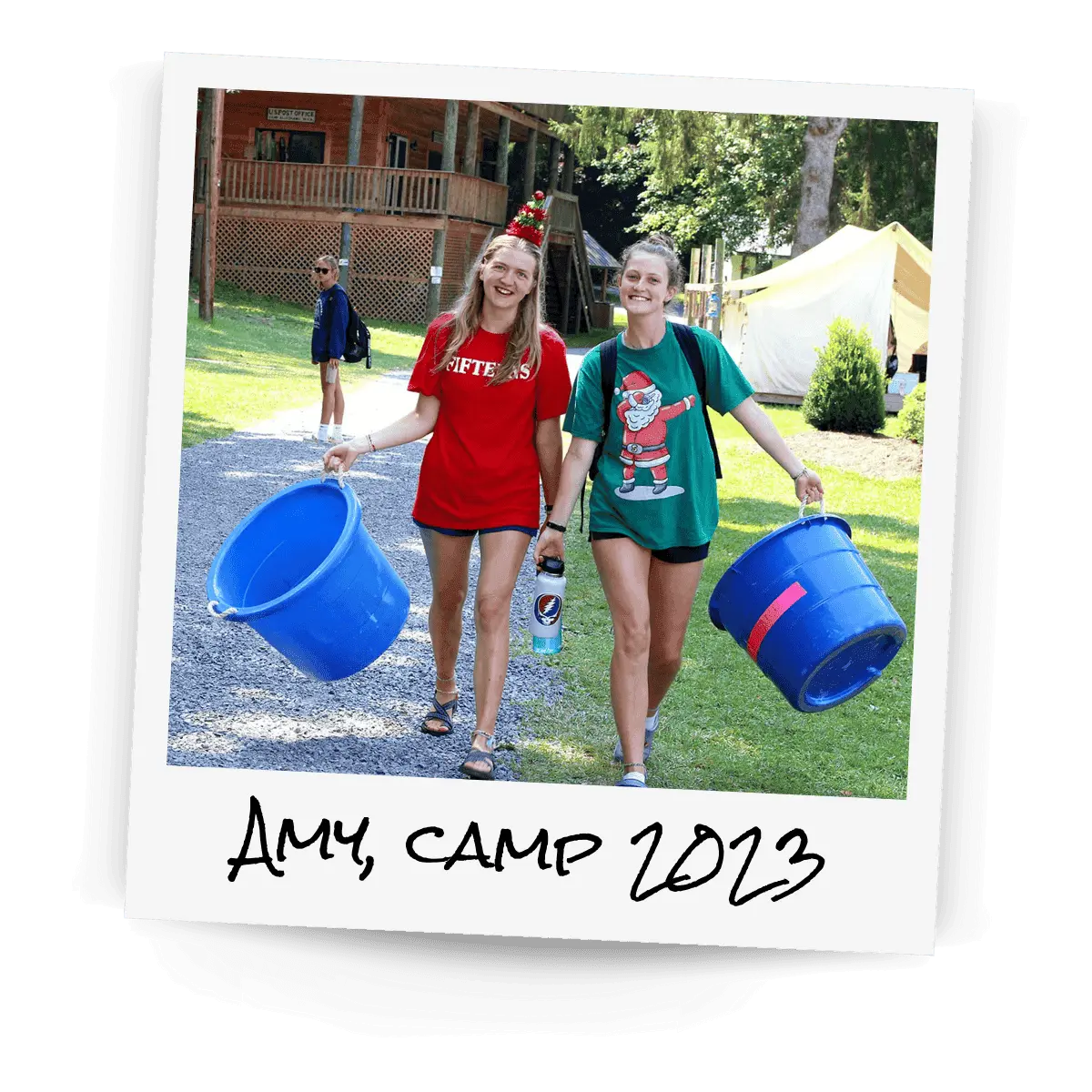 Polaroid of two girls at summer camp in Christmas outfits and accessories carrying two large blue buckets.