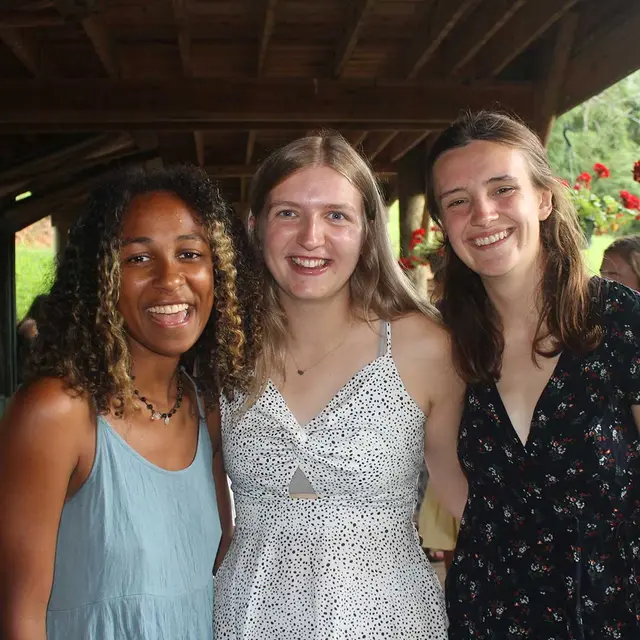 Three girls smile at camera in wooden cabin.