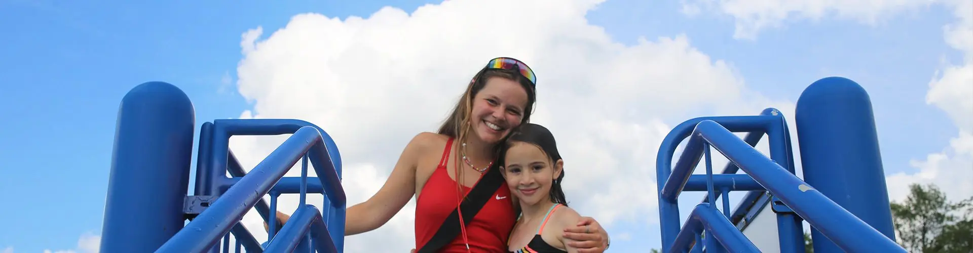 Girl in red wetsuit smile with younger girl on sunny day