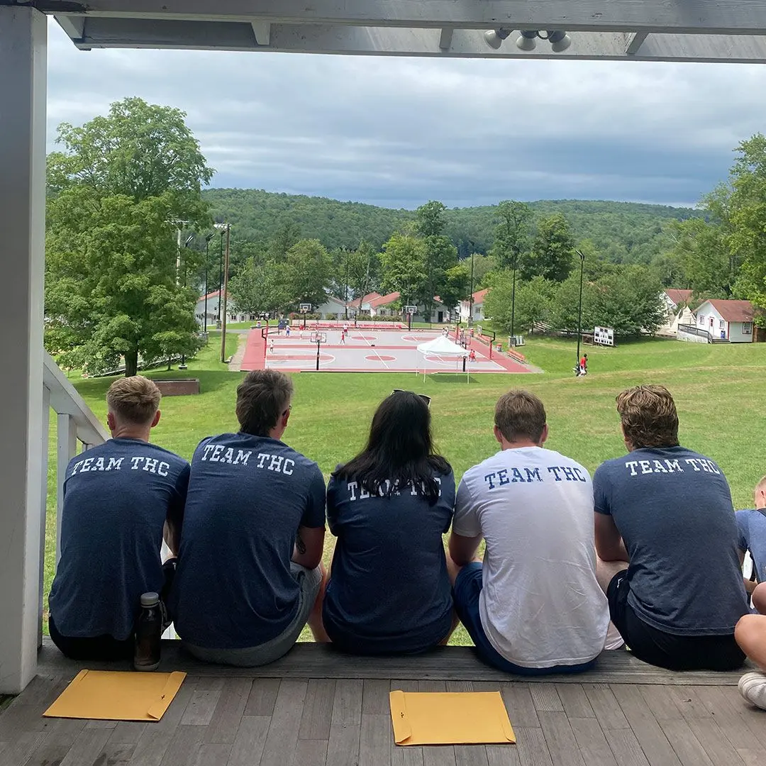 Five camp councelors sit facing away with TEAM THC on their backs