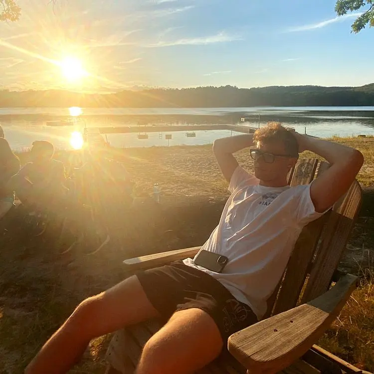 Guy sits in chair beside lake on sunny evening