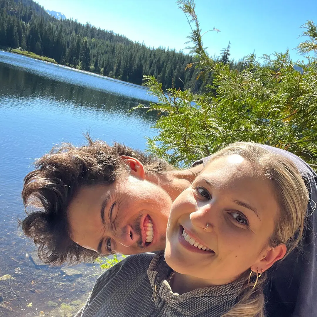 Guy and girl smile at camera beside lake in sunshine