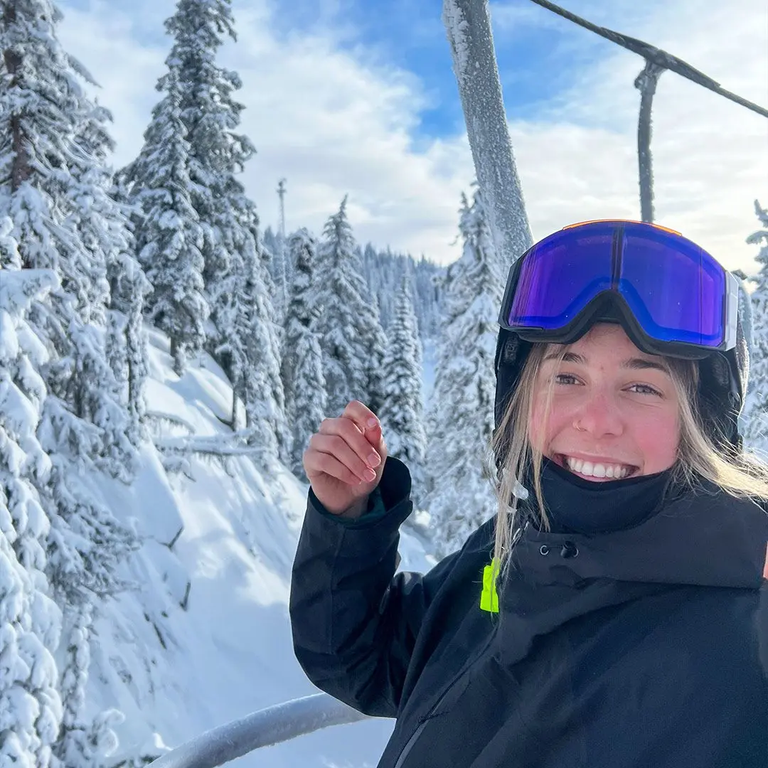 Girl on ski lift smiles for camera on snowy mountain